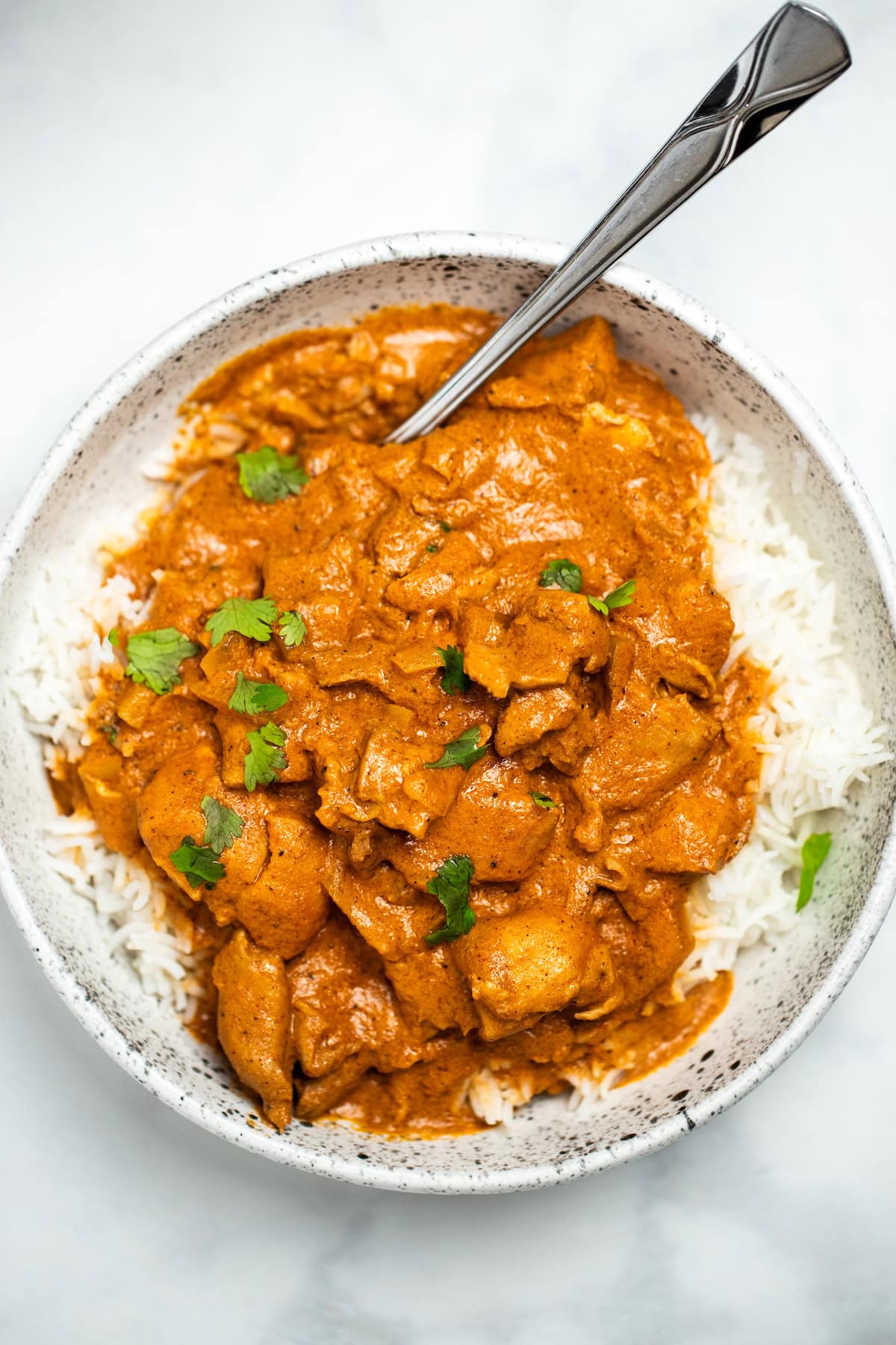 A bowl with basmati rice topped with slow cooker chicken tikka masala and fresh cilantro, with a spoon in the bowl.