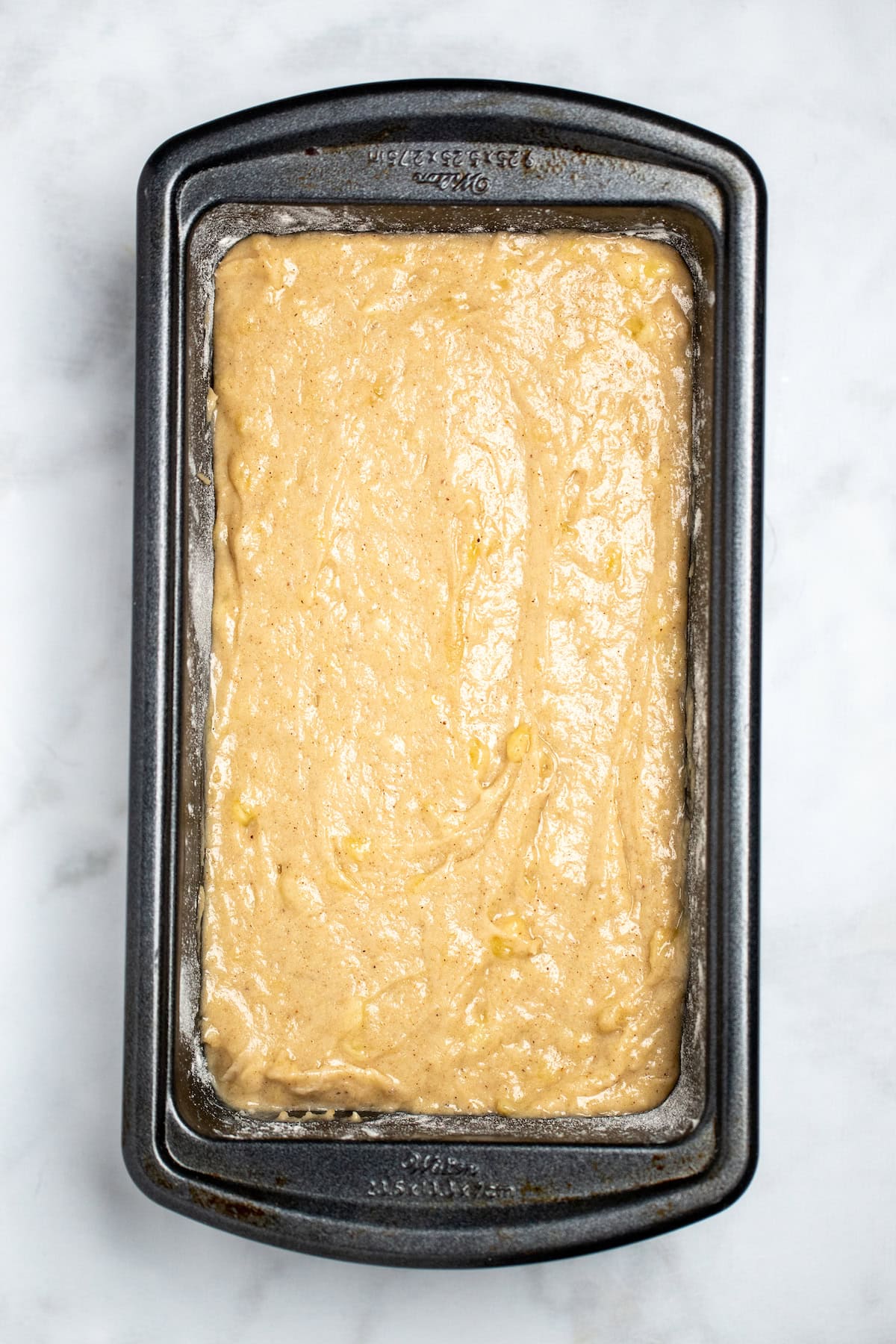 A bread pan full of banana bread batter on a table.