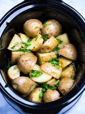 Quartered gold potatoes in a slow cooker topped with fresh parsley.