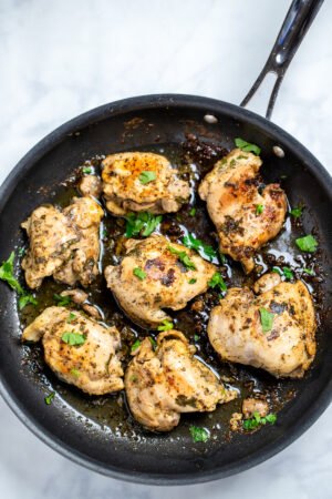 Greek marinated chicken thighs in a skillet topped with fresh parsley.