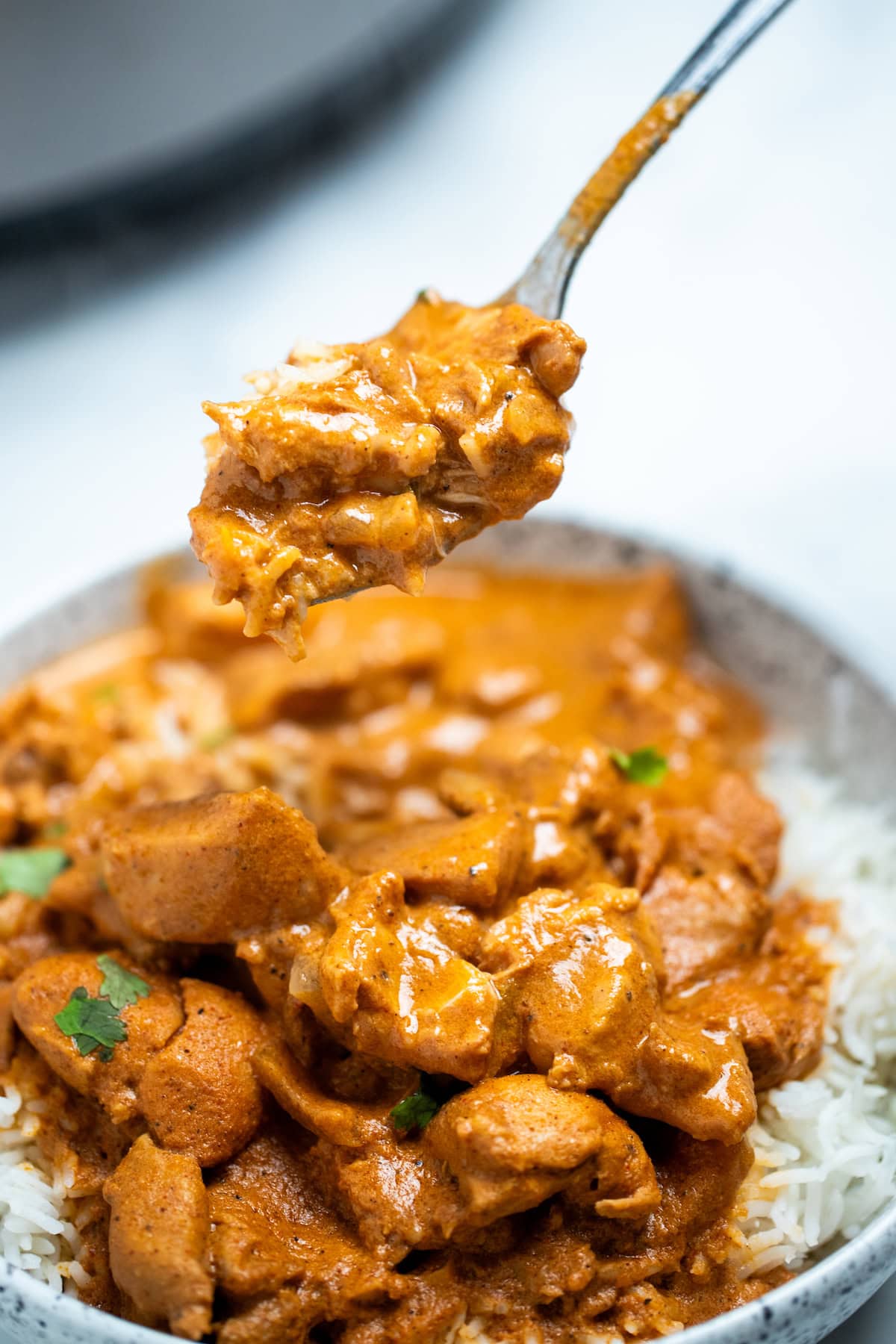 A bowl of slow cooker chicken tikka masala over rice, topped with fresh cilantro pieces, with a spoon lifting some out of the bowl.