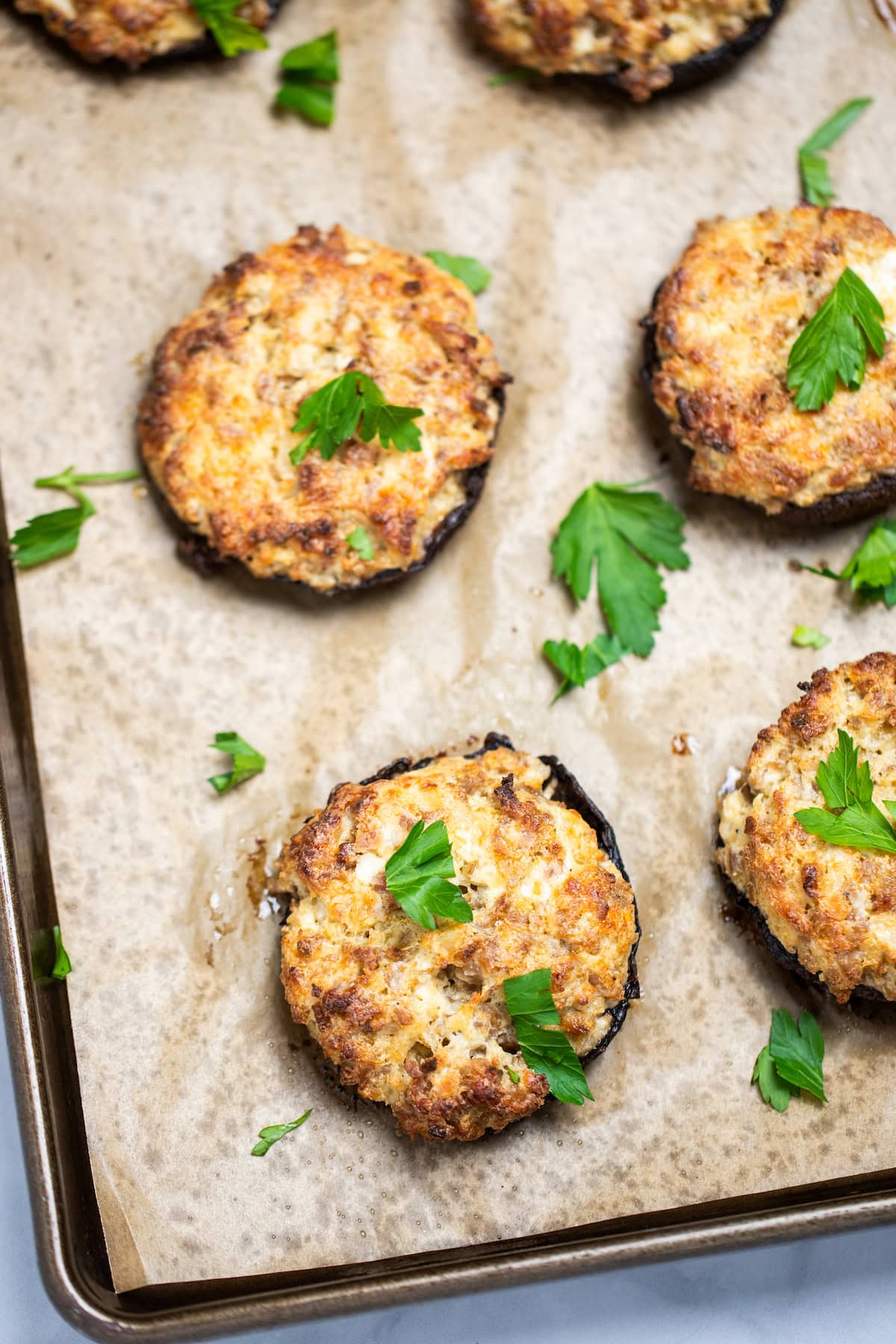 Stuffed portobello mushrooms on a sheet pan with parchment paper, topped with fresh chopped parsley.