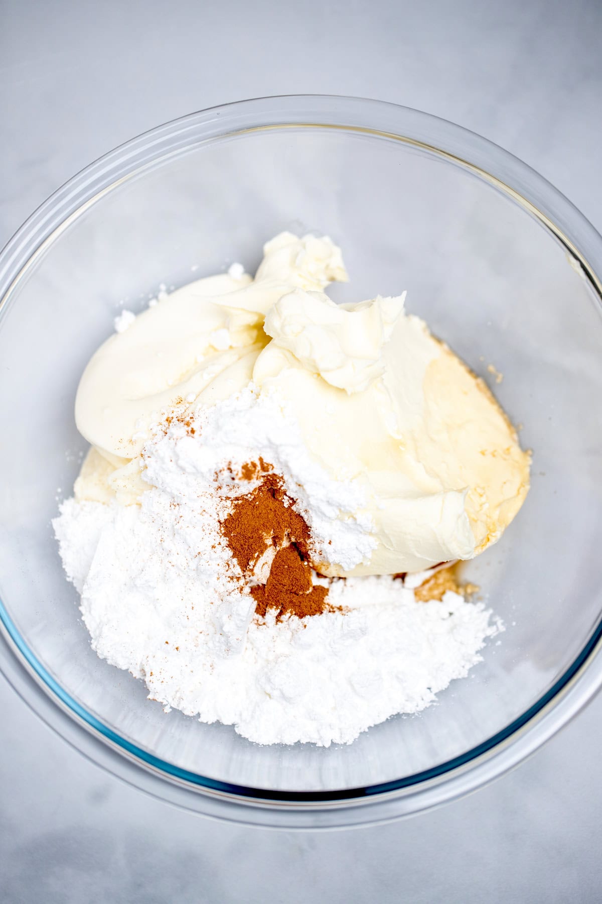 A mixing bowl on a table, full of ricotta cheese, mascarpone cheese, powdered sugar, vanilla extract, and cinnamon.