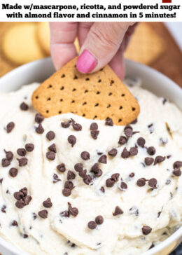 Pinterest pin with a bowl of cannoli dip topped with mini chocolate chips, with a hand using a graham cracker to scoop up some dip. The bowl is sitting on a cutting board surrounded by graham crackers, blueberries, and vanilla wafers.