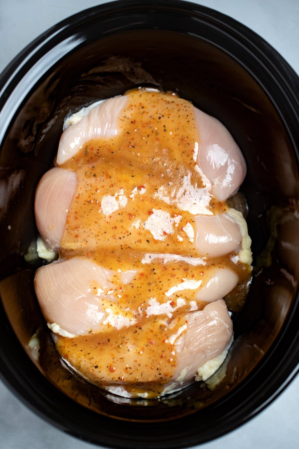A crockpot with raw chicken breasts side by side, topped with Italian salad dressing.