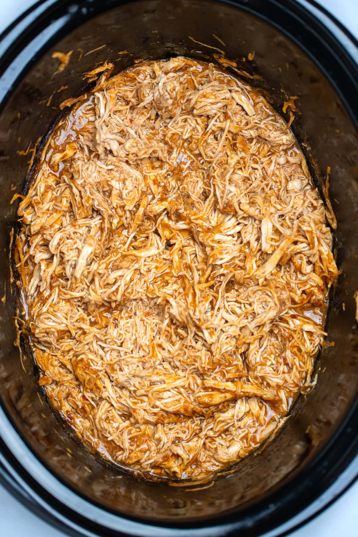 A slow cooker with saucy shredded BBQ chicken ready to be served.