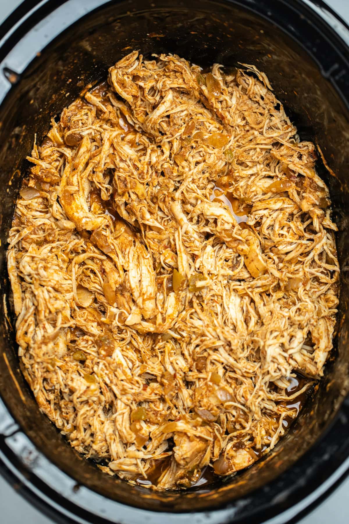 A slow cooker with cooked shredded chicken in a seasoned taco sauce.