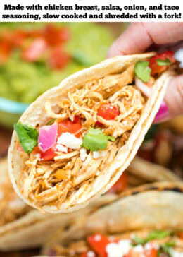 Pinterest pin with a hand holding a taco in a corn tortilla topped with tomato, red onion, queso fresco, and cilantro, above a cutting board with more tacos and a bowl of guacamole.