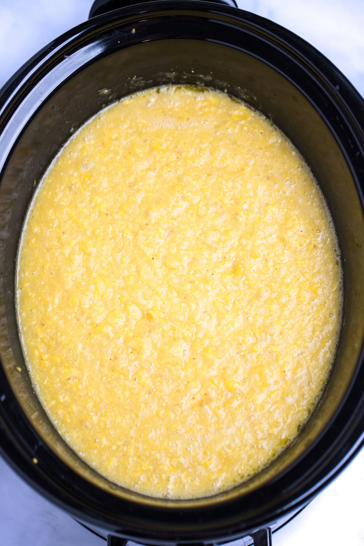 A slow cooker with pureed corn chowder before adding cream.