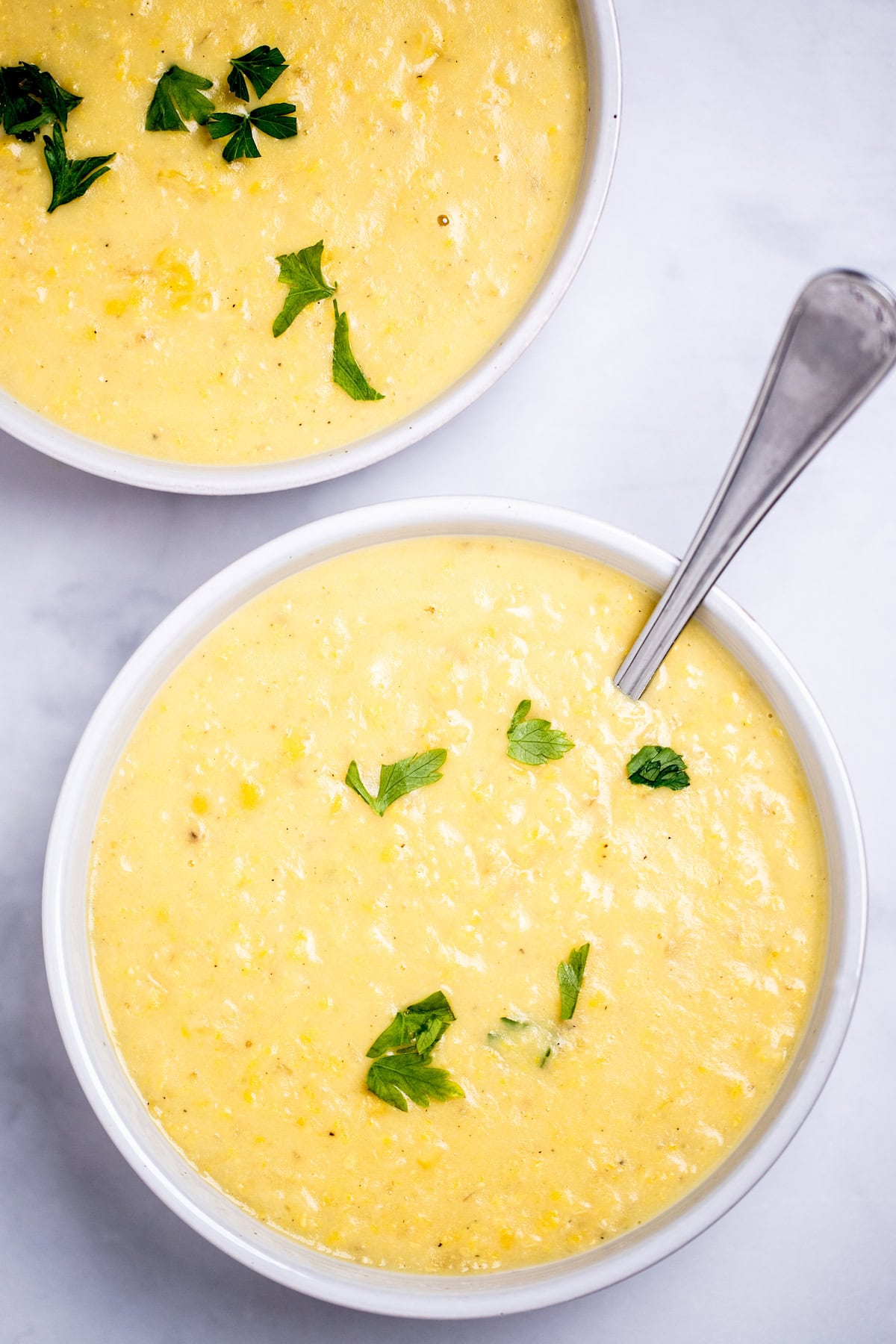 Two bowls on a table filled with corn chowder, topped with fresh parsley with a spoon in the front bowl.