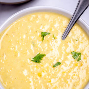 Two bowls on a table filled with corn chowder, topped with fresh parsley with a spoon in the front bowl.