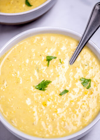 Two bowls on a table filled with corn chowder, topped with fresh parsley with a spoon in the front bowl.