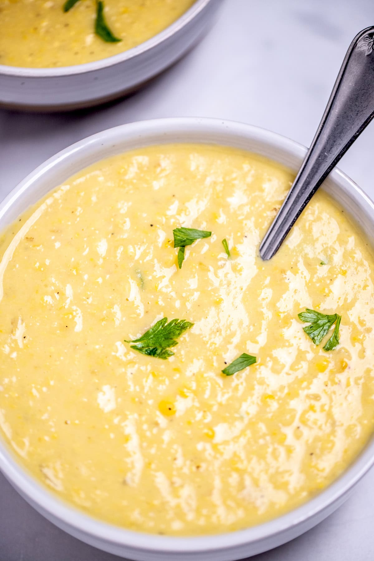 Two bowls on a table filled with corn chowder, topped with fresh parsley with a spoon in the front bowl.