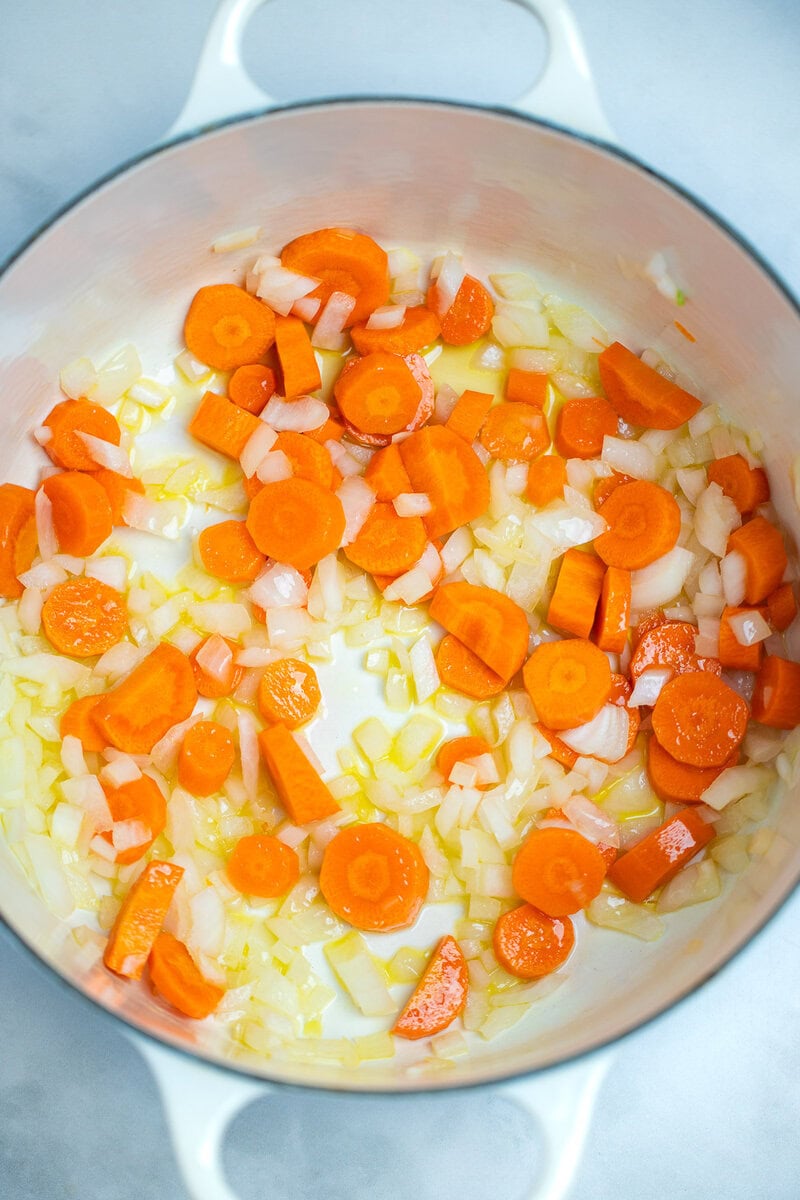 A dutch oven with olive oil, carrots, and onions cooking.