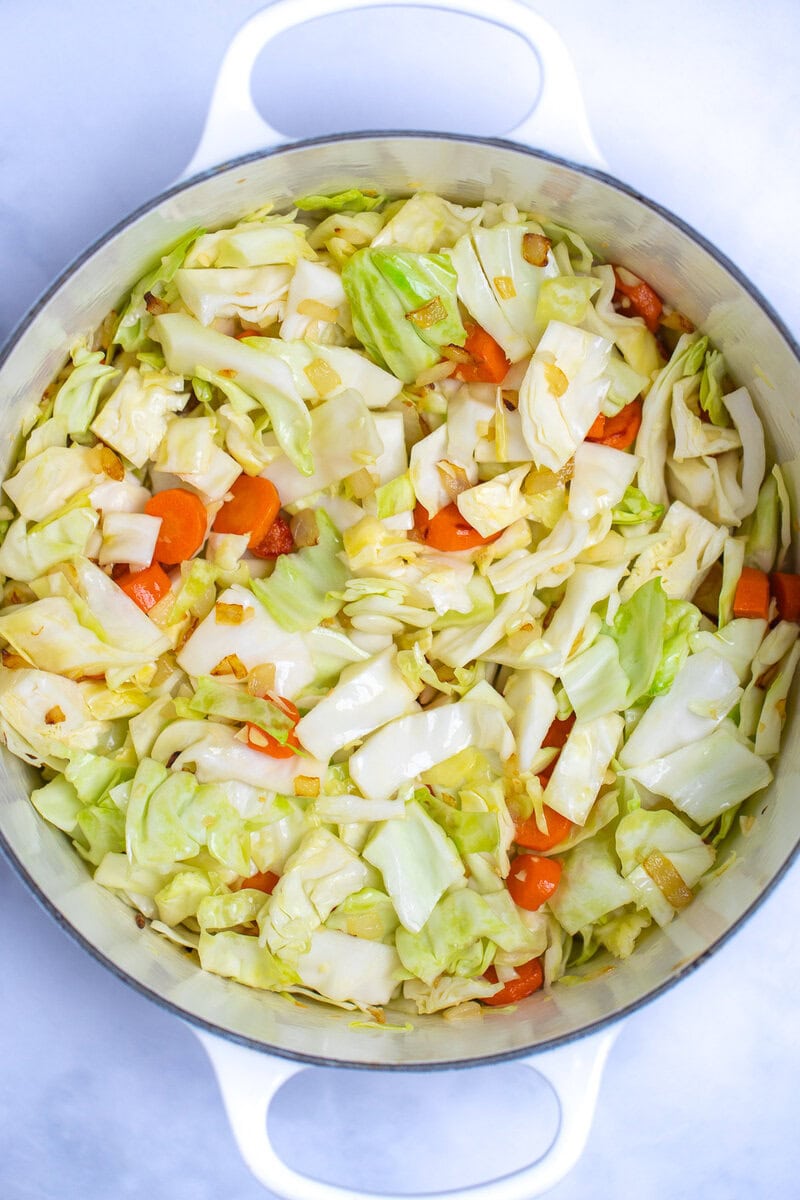 A dutch oven full of cabbage, carrots, onions, and garlic before adding other ingredients.