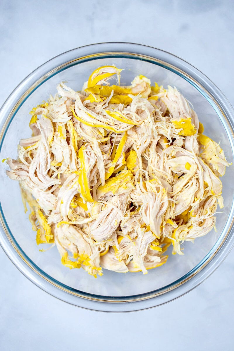 A glass bowl full of shredded chicken on a table.