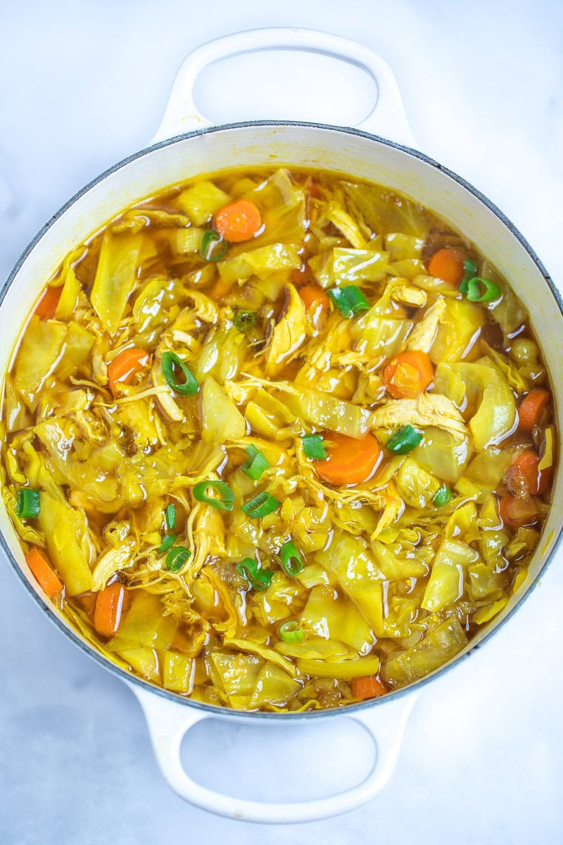 A dutch oven full of cabbage chicken soup topped with green onions on a table.