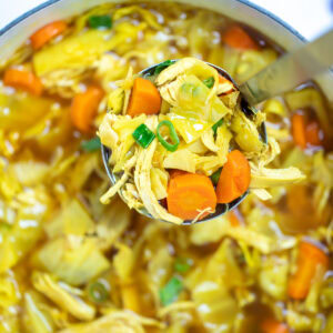 A dutch oven full of cabbage chicken soup topped with green onions, and a ladle scooping up the soup.