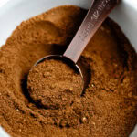 A small bowl with a tablespoon scooping some pumpkin pie spice up.