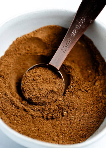 A small bowl with a tablespoon scooping some pumpkin pie spice up.