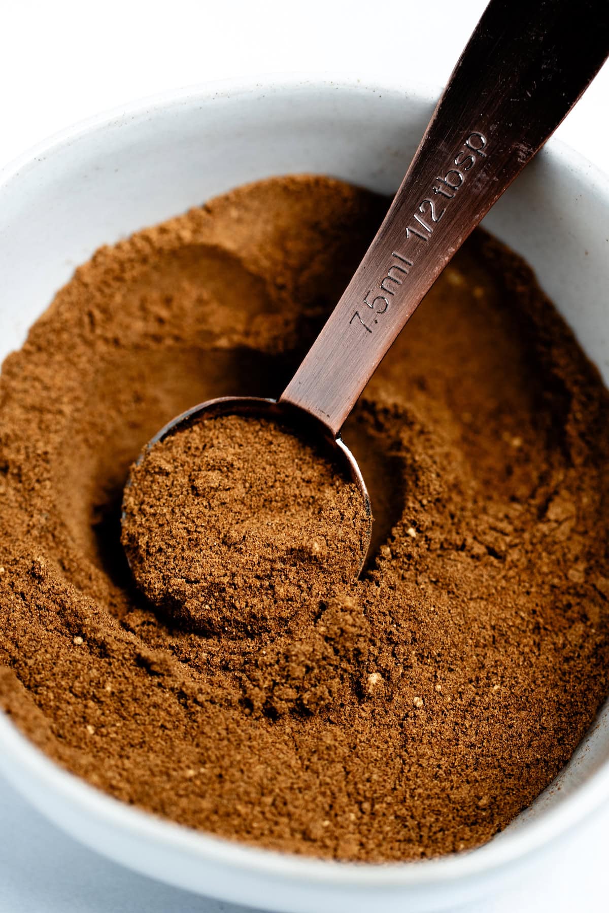 A small bowl with a tablespoon scooping some pumpkin pie spice up.