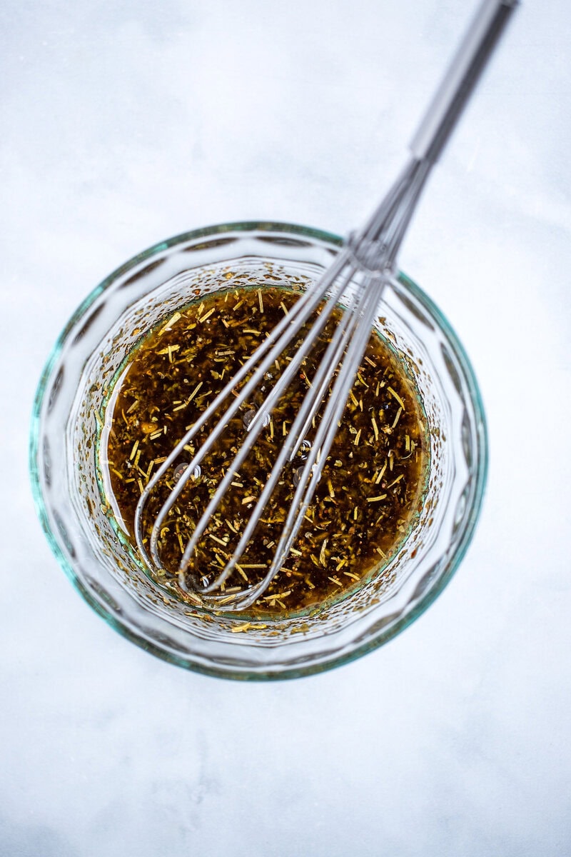 A small bowl on a table with olive oil, balsamic vinegar, and Italian seasoning mixed together with a whisk in the bowl.