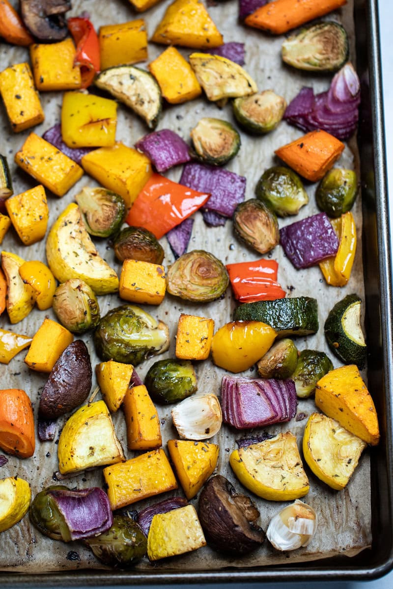 Roasted vegetables on top of parchment paper on a sheet pan, just out of the oven.