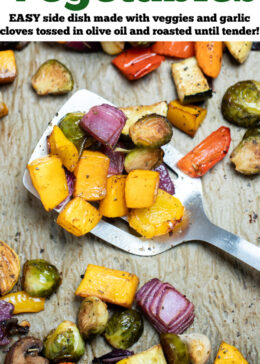 Pinterest pin with roasted vegetables on top of parchment paper on a sheet pan, with a spatula in the middle lifting some vegetables up, just out of the oven.