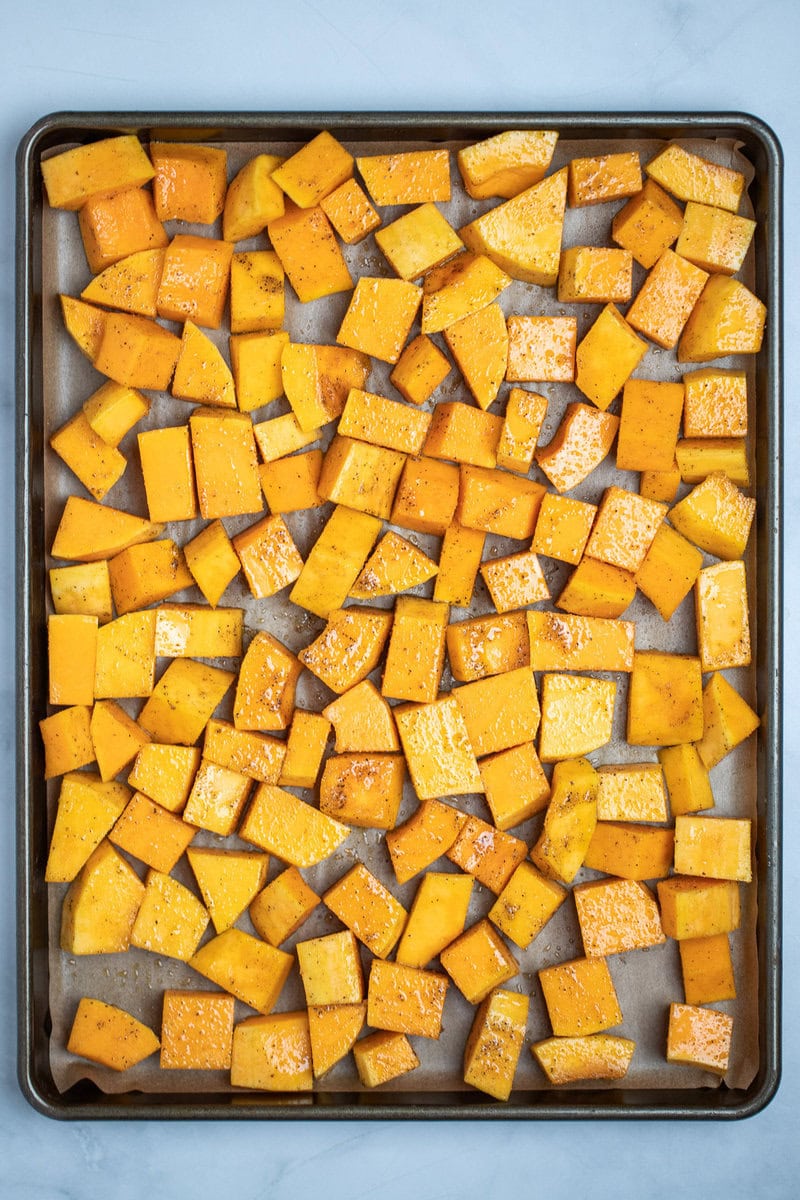 A sheet pan lined with parchment paper, with prepared butternut squash in a single layer, before being roasted.