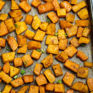 A sheet pan lined with parchment paper with a single layer of roasted butternut squash, topped with green onions.