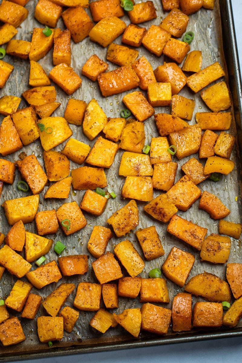 A sheet pan lined with parchment paper with a single layer of roasted butternut squash, topped with green onions.