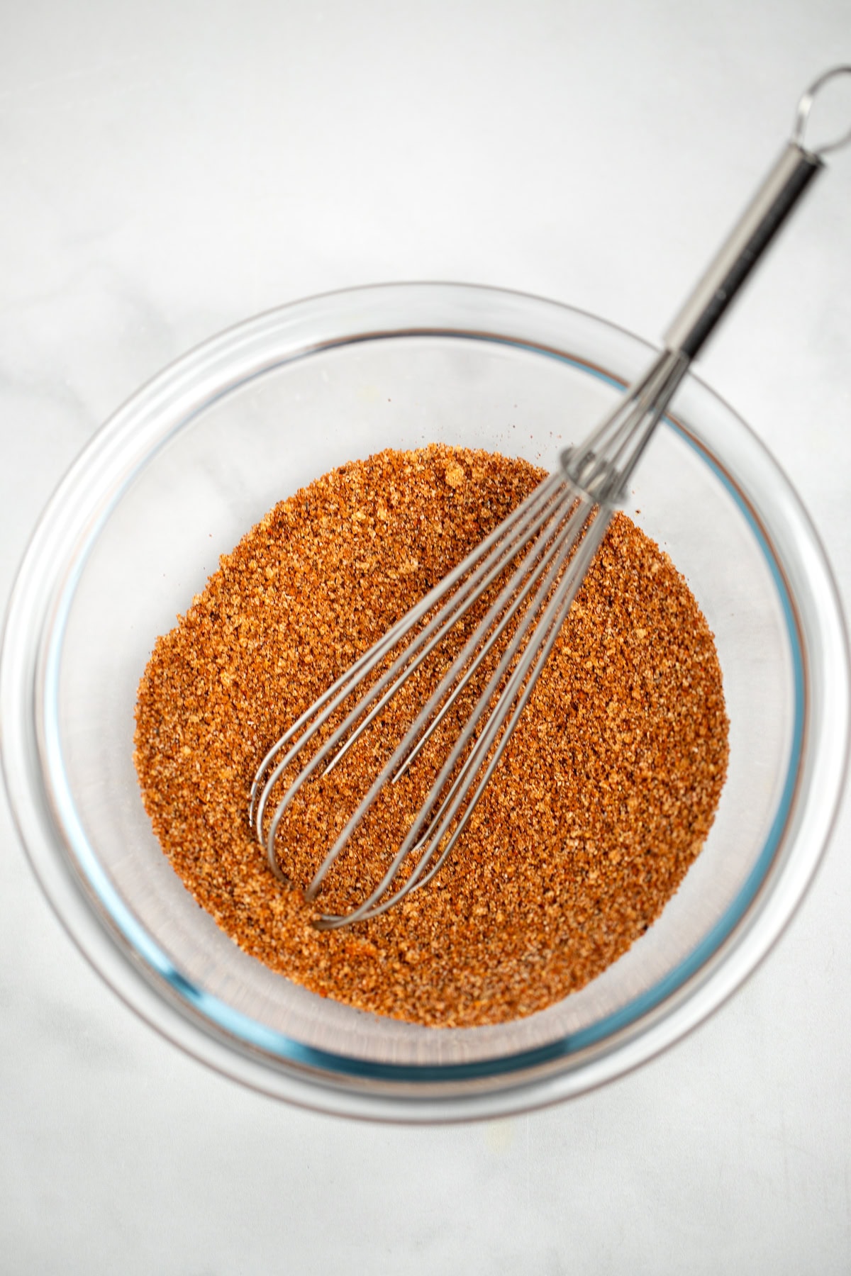 A small glass bowl with a whisk full of pork rub spices.