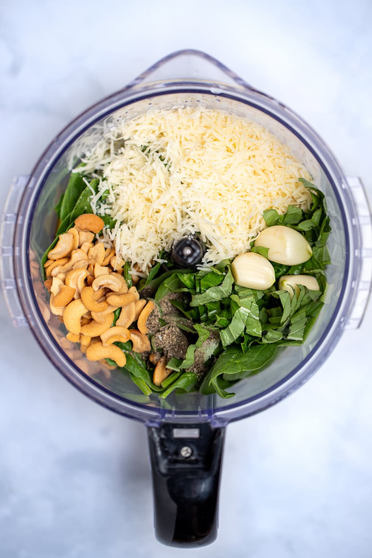 A food processor with all of the ingredients for spinach pesto inside before being blended, with no lid on the processor.