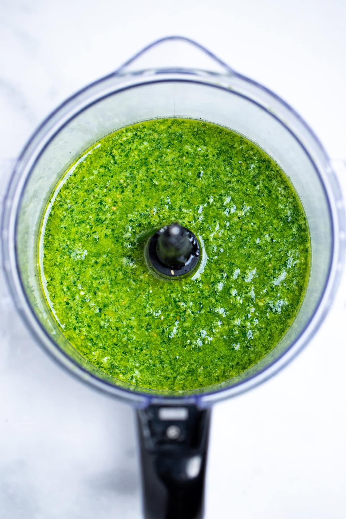 A food processor without the lid, full of blended spinach pesto.