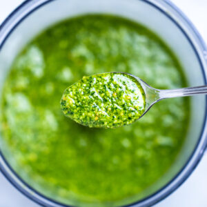 A spoon lifting some spinach pesto out of the food processor.