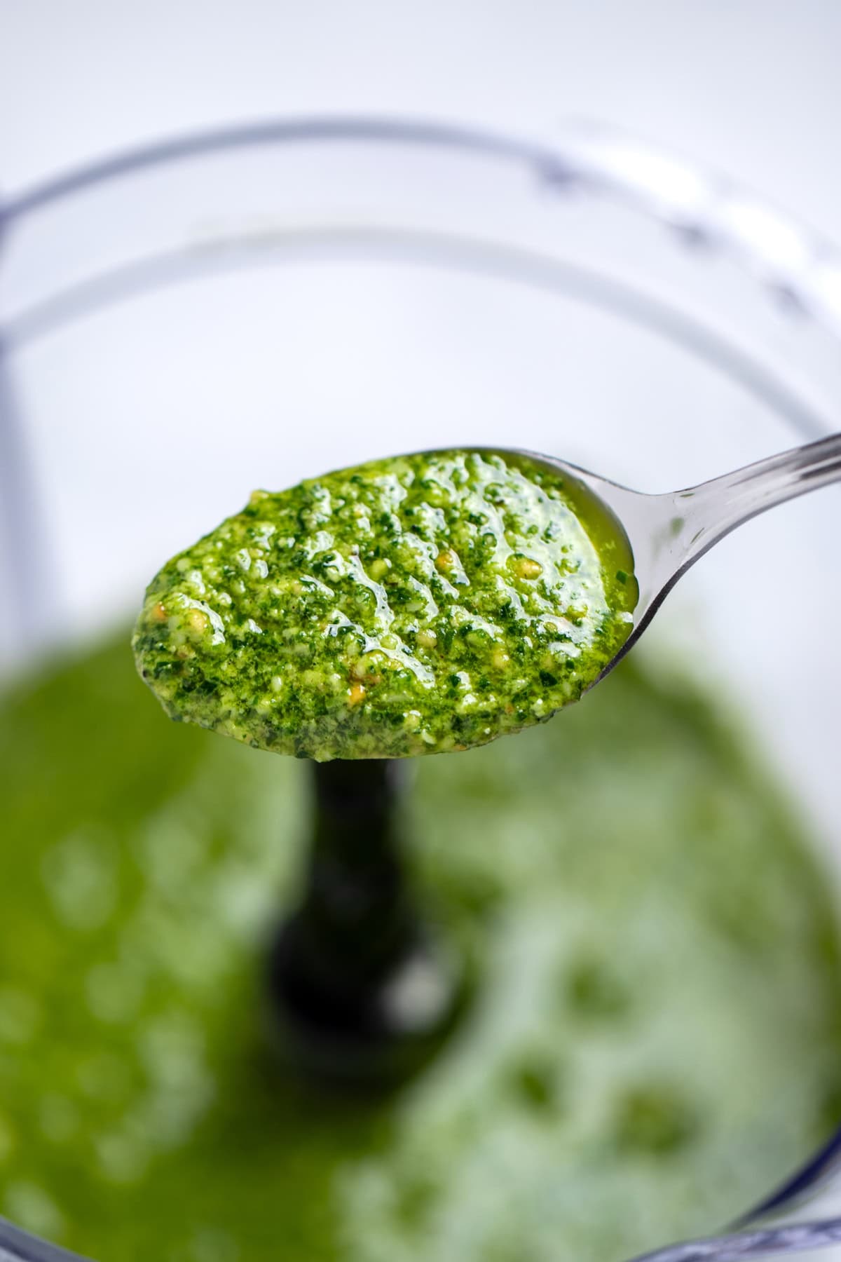 A spoon lifting some spinach pesto out of the food processor.