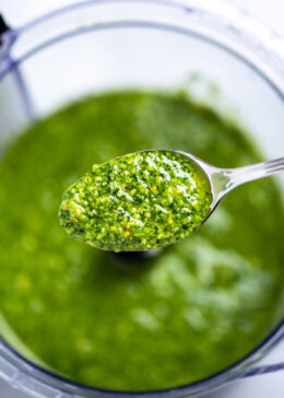 A spoon lifting some spinach pesto out of the food processor.