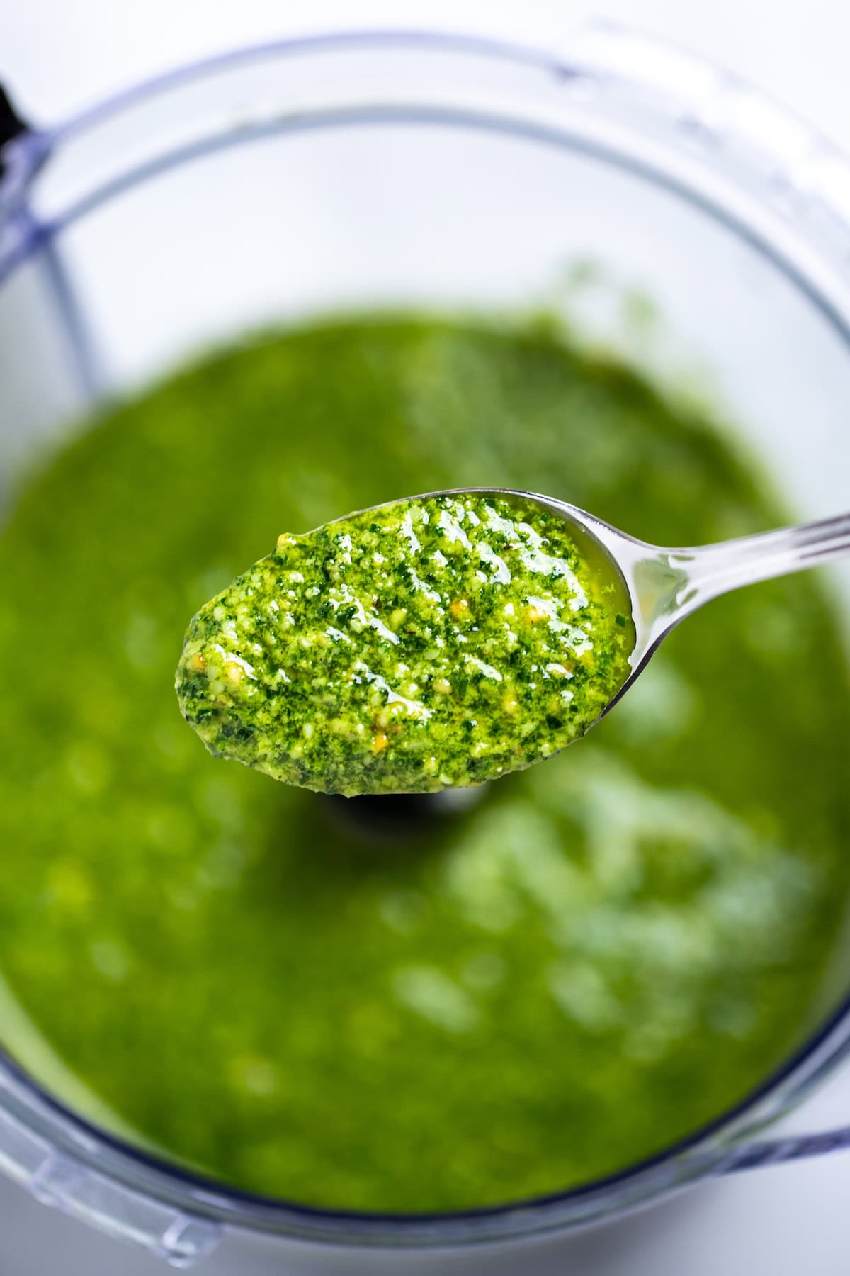 A spoon lifting some spinach pesto out of the food processor.