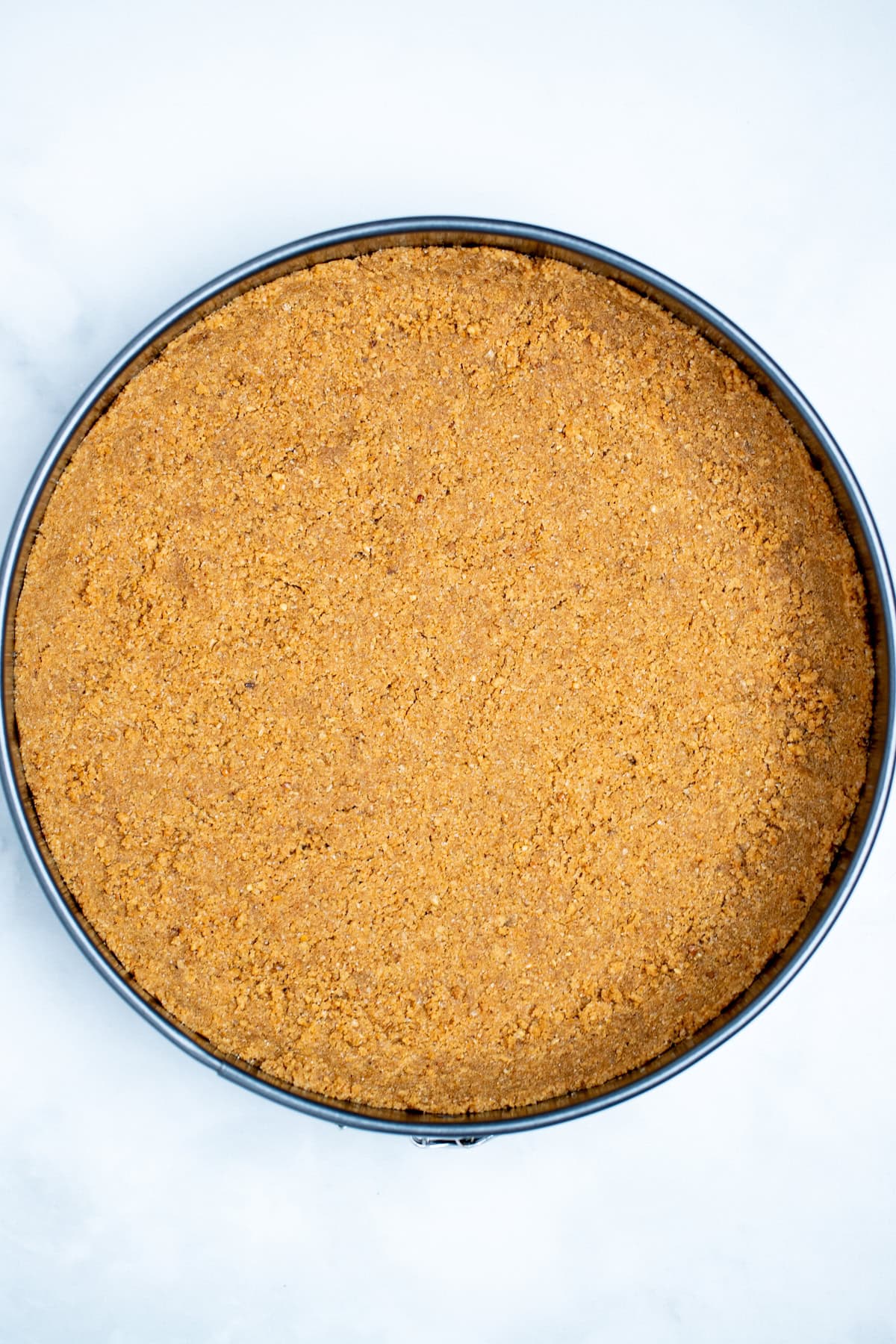 A springform pan with a graham cracker crumb mixture pressed into the bottom of the pan.