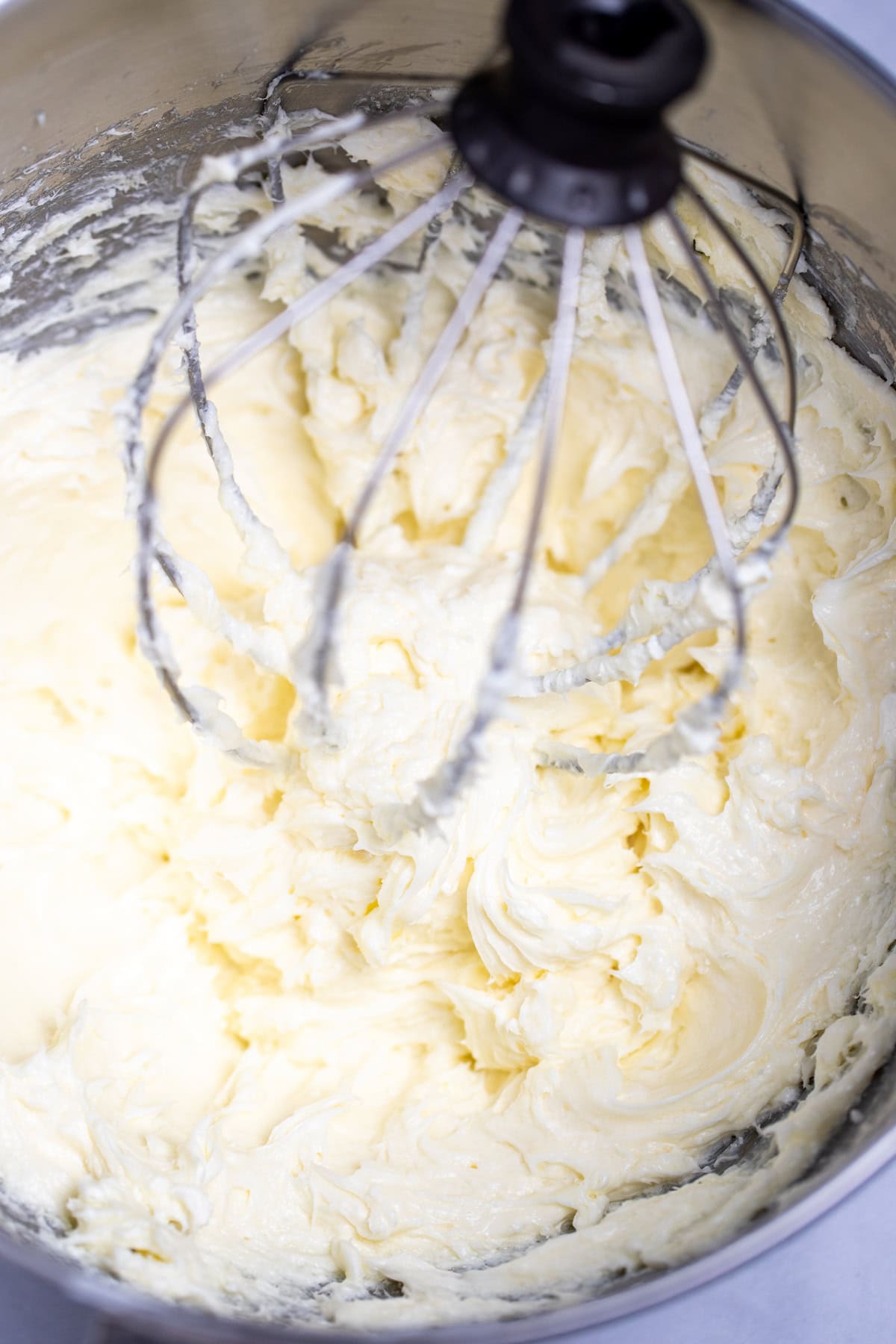 A stand mixer bowl with cream cheese and sugar mixed together, with the whisk attachment in the bowl.