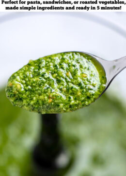 Pinterest pin with a spoon lifting some spinach pesto out of the food processor.