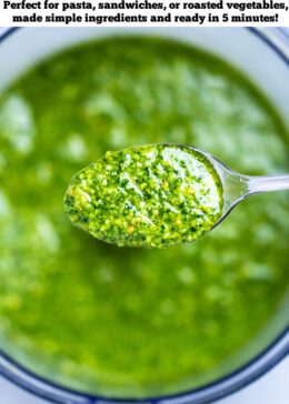 Pinterest pin with a spoon lifting some spinach pesto out of the food processor.