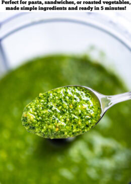 Pinterest pin with a spoon lifting some spinach pesto out of the food processor.