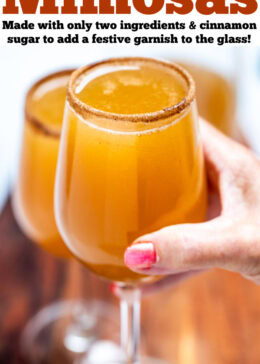 Pinterest pin with a hand holding a wine glass filled with apple cider mimosas, with another wine glass on a cutting board in the background.