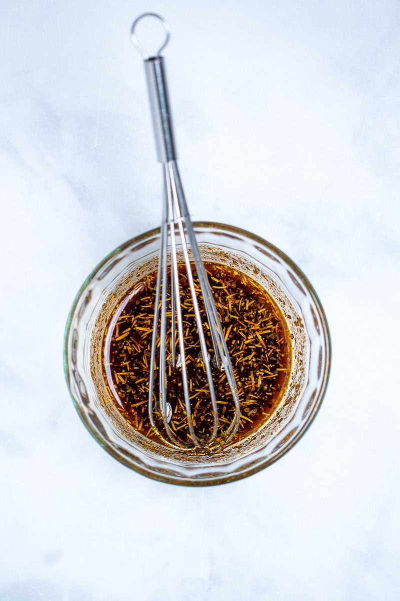 A small glass bowl with olive oil and seasoning whisked together, with a whisk in the bowl.