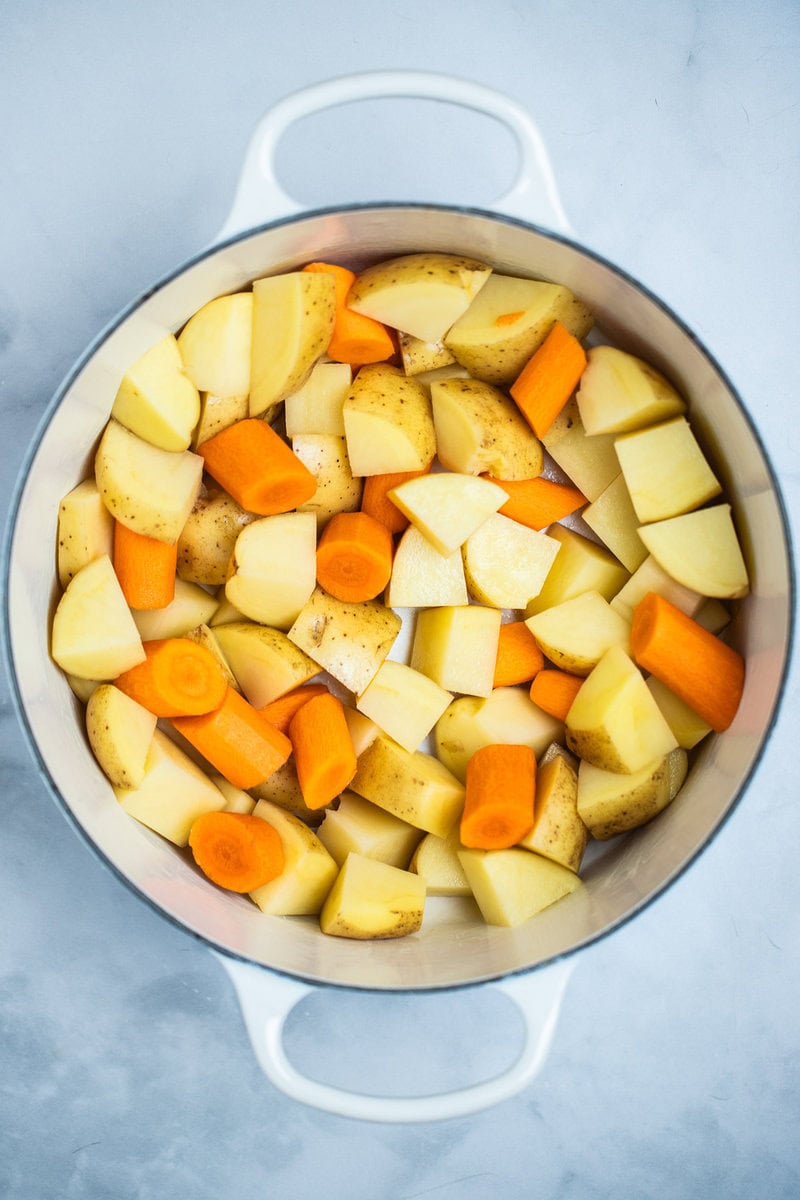 A dutch oven with uncooked chopped potatoes and carrots.