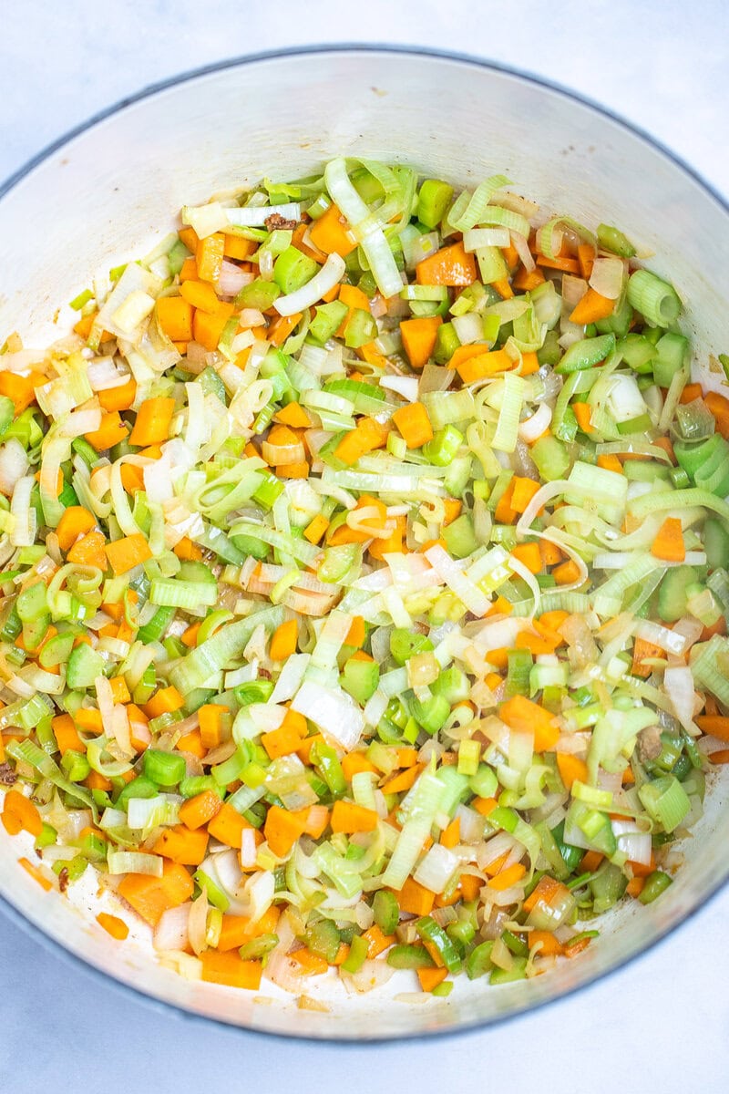 A dutch oven with softened leeks, onion, carrots, and celery.