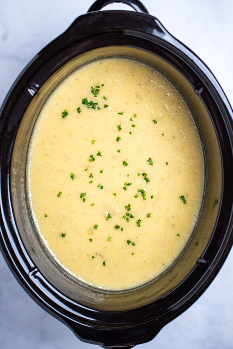 A slow cooker full of potato soup topped with chives.