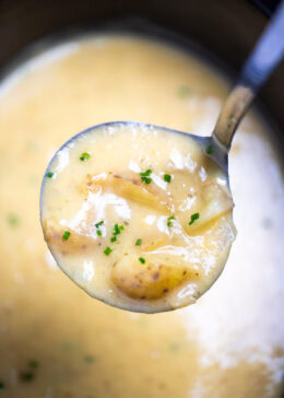 A ladle lifting some potato soup out of the slow cooker.