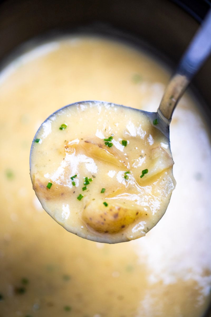 A ladle lifting some potato soup out of the slow cooker.